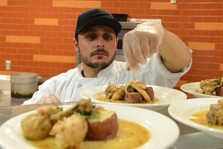 Culinary student topping a potato dish with fresh cut herbs.