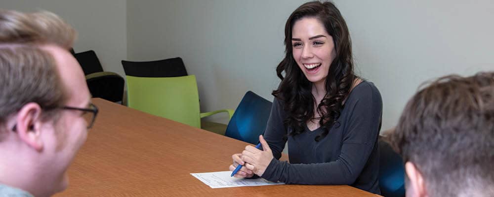 An FLCC student sits behind a long conference table. She shares a laugh with two other people in the room.